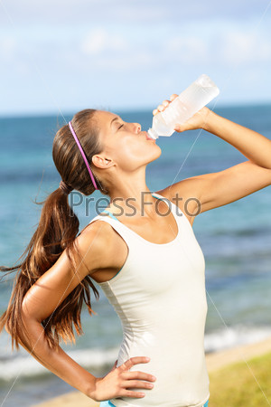 Fitness woman drinking water after beach running