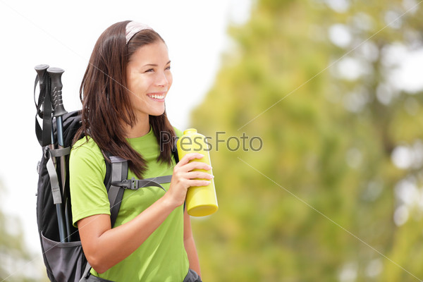 Hiker woman smiling happy drinking water. Female hiking in forest looking to the side. Beautiful multiracial Asian Caucasian female model outdoors in nature.