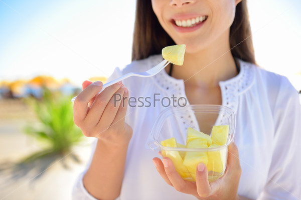 Pineapple - woman eating sliced Hawaiian pineapple fruit as a healthy snack from take away bowl.