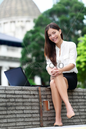 Business woman on laptop in Hong Kong. Businesswoman on computer and internet outside in Central Hong Kong. Young female professional business woman smiling. Asian Chinese Caucasian woman.