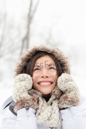 winter woman in snow looking up at copy space outside on snowing cold winter day. Portrait multiethnic Caucasian Asian female model outside in first snow