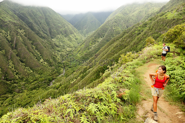 Hiking people on Hawaii, Waihee ridge trail, Maui, USA. Young woman and man hikers walking in beautiful lush Hawaiian forest nature landscape in mountains. Asian woman hiker in foreground.