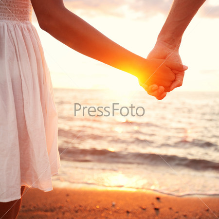 Love - romantic couple holding hands, beach sunset. Lovers or newlywed married young couple in romance on beautiful sunset at beach. Young woman and man in love walking hand in hand on beach.