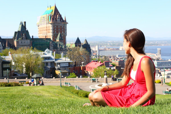 Quebec City scape with Chateau Frontenac and young woman in red summer dress sitting in grass enjoying the view. Tourist or student in Quebec City, Quebec, Canada.