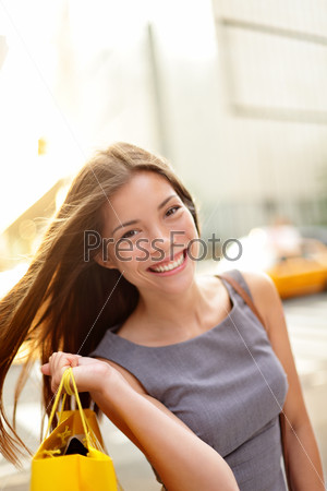 Shopping woman on Manhattan, New York City.  Shopper smiling happy outdoor in streets of New York. Fresh blissful mixed race Asian / Caucasian girl holding shopping bag with yellow taxi cab.
