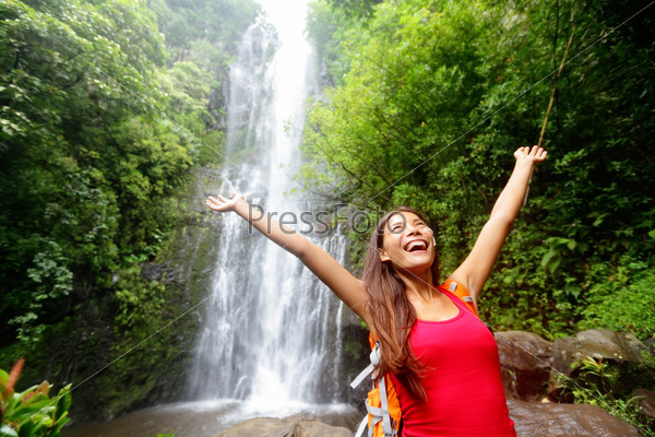 Hawaii woman tourist excited by waterfall during travel on the famous road to Hana on Maui, Hawaii. Ecotourism concept image with happy backpacking girl. Mixed race Asian / Caucasian backpacker.