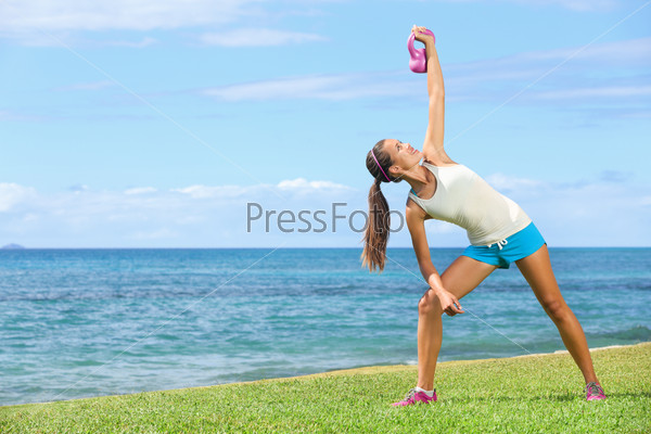 Fitness exercise woman using kettlebell in fitness strength training workout outside on grass by the ocean. Beautiful young fit instructor and fitness model.