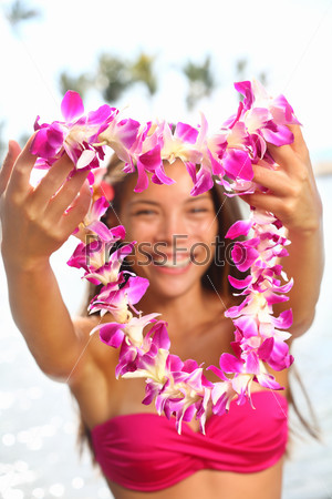 Hawaii woman showing flower lei garland of pink orchids. Beautiful smiling mixed race woman in bikini on beach giving a welcoming Lei on the hawaiian island Big Island.