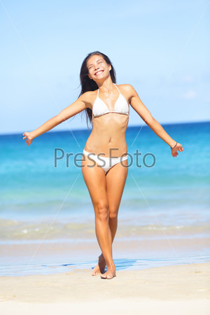 Beach summer holidays bikini woman walking. Carefree freedom in summer sun on tropical beach on sunny day. Full length portrait of ethnic model.