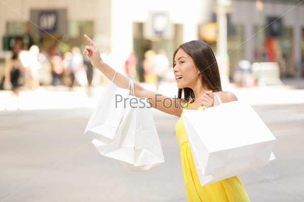 Shopping woman in New York City looking for yellow taxi cab. Beautiful happy summer shopper holding shopping bags walking outside smiling. Multiracial Asian Caucasian model on Manhattan, USA.