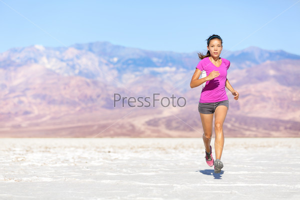 Running sport athlete woman sprinting in trail run in desert.\
Female fitness runner in sprint workout training in shorts and\
t-shirt. Fit muscular girl sport model outside under blue\
sky.