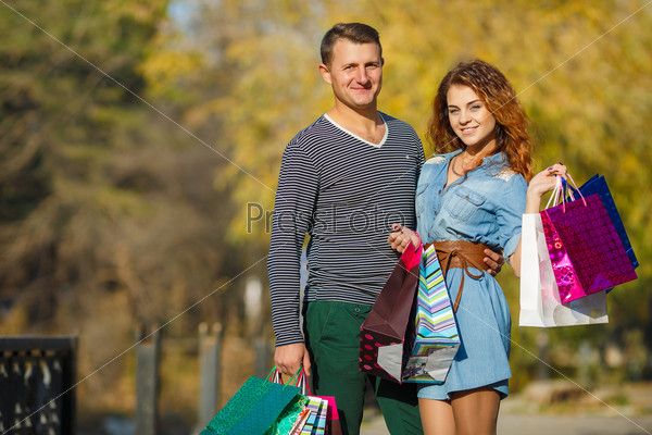 Portrait of happy couple with shopping bags. Couple with paper bags full of presents doing shopping. Outdoor. In park