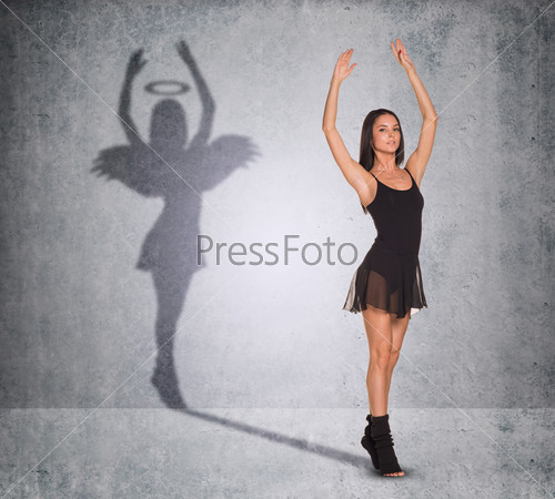 Ballet dancer with shadow showing angel side with wings and nimbus on wall texture background, looking at camera