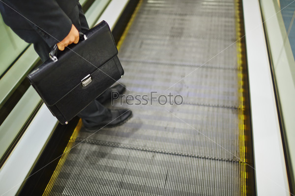 Close-up of legs of businessman with briefcase descending on escalator