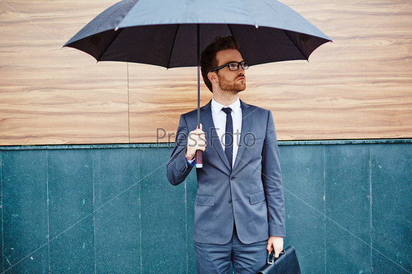 Young entrepreneur with briefcase standing outside under umbrella
