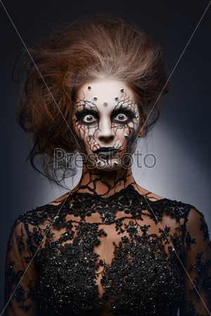 A girl standing like a statue in a creepy halloween costume of a witch with peircing and cracked face paint. Creepy statue.