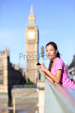 London woman runner listening to music on smartphone near Big Ben. Female running girl resting after training in city. Fitness girl smiling happy on Westminster Bridge, London, England, United Kingdom