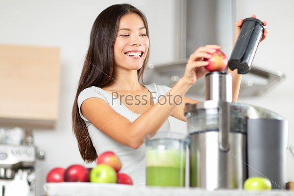 Juicing - woman making apple and green vegetable juice using juicer machine at home in kitchen. Healthy eating happy woman making green vegetable and fruit juice. Mixed race Asian Caucasian model.