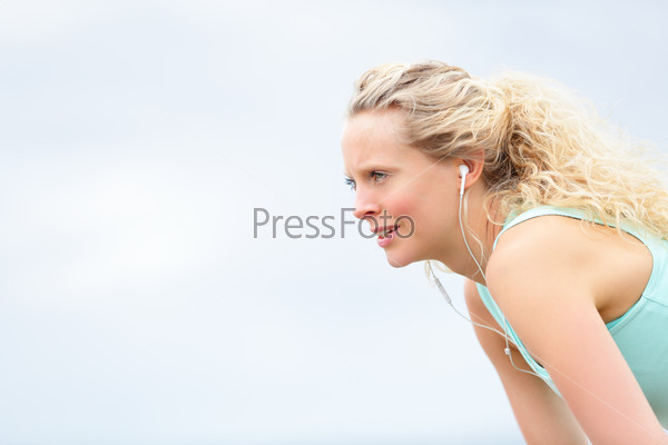 Runner woman resting after running workout outside. Beautiful blonde female athlete relaxing tired after jogging exercise training outdoors. Girl listening to music in earphones.