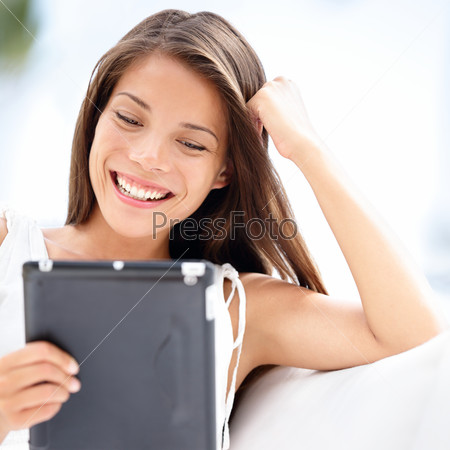 Tablet computer. Pretty young asian caucasian woman holding black tablet reading ebook relaxed in sofa
