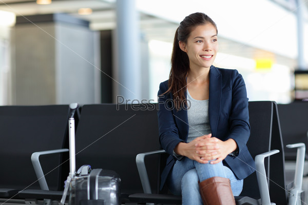 Passenger. Asian woman in airport waiting for air travel. Young business woman smiling sitting with travel suitcase trolley, in the waiting hall of the departure lounge of an international airport.