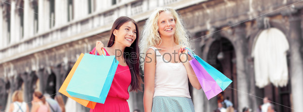 Shopping women banner. Happy shoppers holding shopping bags having fun laughing. Two beautiful young Asian and Caucasian woman girlfriends on travel vacation, Piazza San Marco Square, Venice, Italy