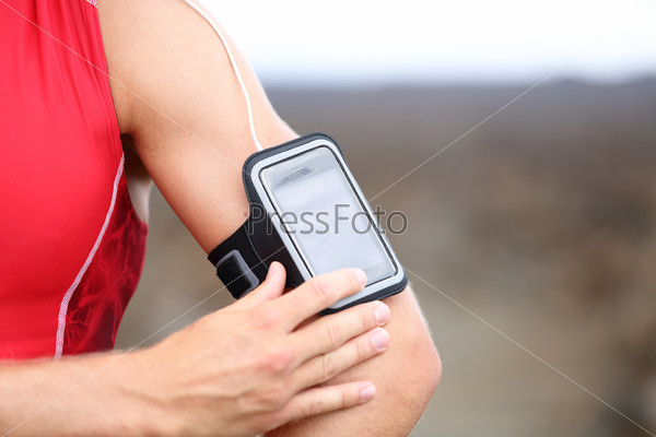 Smart phone running music closeup - male runner listening to music adjusting settings on armband for smartphone. Fit man fitness model working out outside in red sporty outfit.