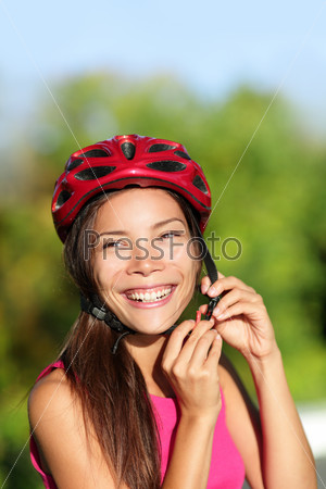 Biking helmet - woman putting bicycle helmet outside. Asian girl on bike, close up of helmet and face. Beautiful mixed race Caucasian Asian female outside.