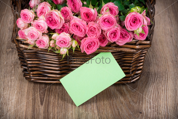 Roses in the basket and a greeting card on wooden background