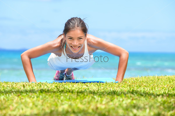 Push-ups fitness woman doing pushups outside on beach on grass. Fit female sport model girl training crossfit outdoors. Mixed race Asian Caucasian athlete in her 20s.