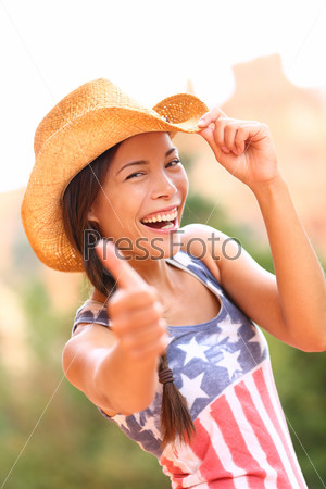 American cowgirl woman happy excited giving thumbs up wearing cowboy hat outdoors in countryside. Cheerful elated joyful woman smiling enjoying freedom. Beautiful multiracial Asian Caucasian female.