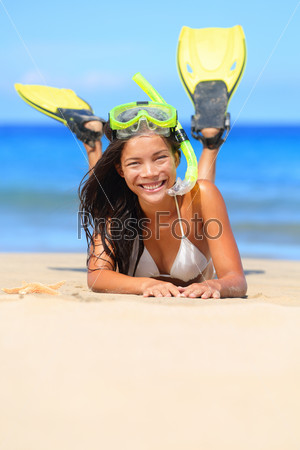 Travel woman on beach vacation with snorkel lying in sand with snorkeling mask and fins smiling happy enjoying the sun on sunny summer day. Multi ethnic Asian Chinese / Caucasian woman model.