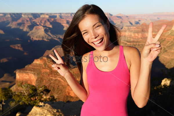 Asian hiker - hiking woman portrait at Grand Canyon. Hiker woman smiling showing victory v hand sign in happy outdoor portrait. Aspirational lifestyle image of female hiker in Arizona, USA.