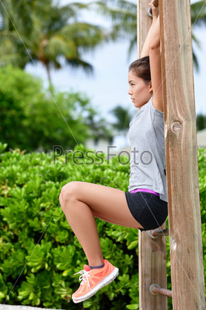 Fitness woman workout doing abs exercises on outdoor beach gym. Asian girl training abs by raising legs on a vertical bars rack during a fitness station circuit routine.