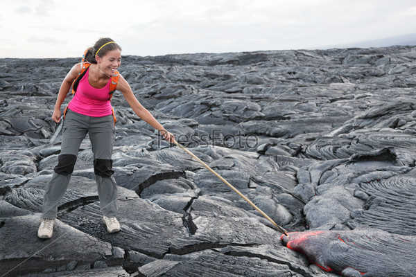 Hawaii Big Island lava tourist on volcano poking stick in red hot moving lava. flowing lava from Kilauea volcano around Hawaii volcanoes national park, USA. Young asian woman hiker.