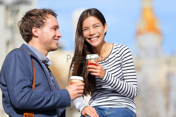 Happy couple drinking coffee talking flirting having fun together. Happy urban young man and woman laughing relaxing outside with disposable coffee cup. Caucasian Asian Interracial couple.
