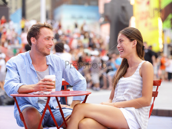Dating couple, New York, Manhattan, Times Square dating\
drinking coffee smiling happy sitting at red tables enjoying their\
tourism vacation travel in the USA. Asian woman, Caucasian\
man.