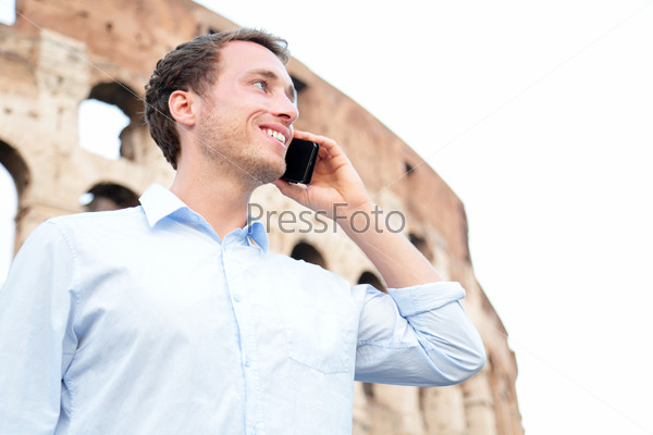 Business man on cell phone, Colosseum, Rome, Italy. Young businessman talking on smartphone outside smiling happy in casual shirt in front of Coliseum. Caucasian male professional in Europe.