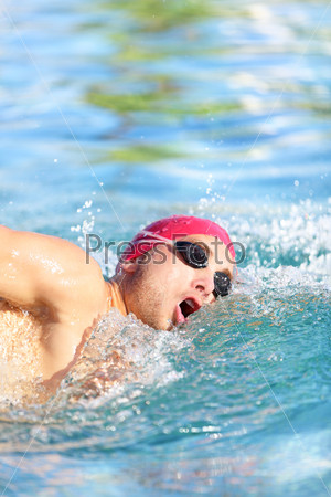 Swimmer man swimming crawl in blue water. Portrait of an athletic young male triathlete swimming crawl wearing a red cap and swimming goggles while. Triathlete training for triathlon.