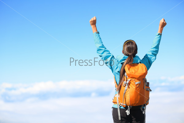 Winner / Success concept. Hiker woman cheering elated and blissful with arms raised in the sky after hiking to mountain top summit above the clouds.