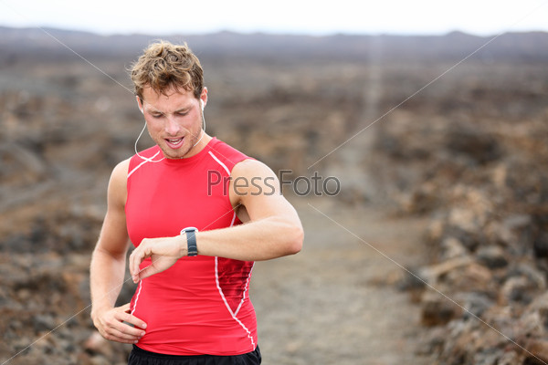 Running athlete man looking at smartwatch heart rate monitor GPS smart watch. Runner listening to music in earphones. Athlete resting tired after training on Big Island, Hawaii, USA.
