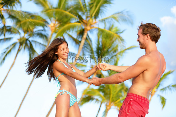 Beach couple fun on vacation dancing playful. Happy young lovers enjoying summer vacation holiday on beach. Beautiful interracial couple in love. Asian woman, Caucasian man on Hawaii.