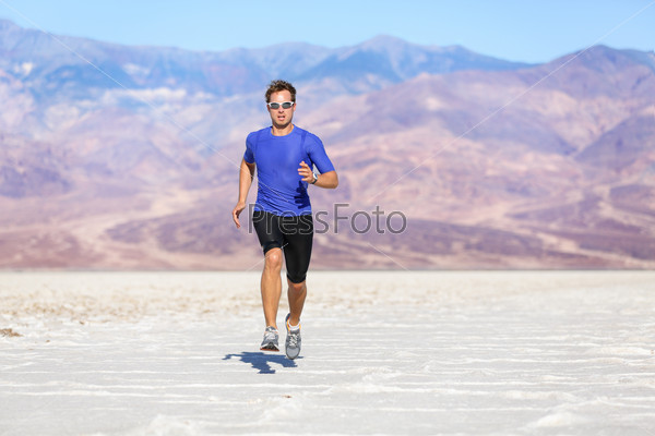 Running man - sprinting athlete runner in desert. Fit athletic male fitness model in fast sprint run at great speed towards camera. Sport in amazing extreme desert landscape.