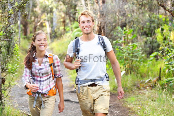 Outdoor activity couple hiking - happy hikers walking in forest. Hiker couple laughing and smiling. Multiracial group, Caucasian man and Asian woman on Big Island, Hawaii, USA.