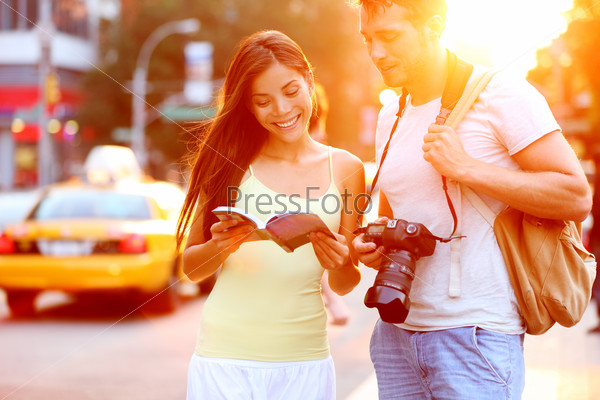 Travel tourist couple traveling in New York reading guide\
book standing with SLR camera at sunset on Manhattan with yellow\
taxi cab in the background. Happy young multiracial couple on\
summer holidays