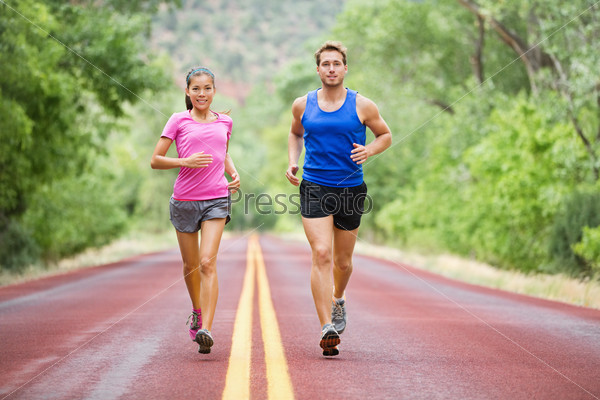 Fitness sport couple running jogging outside on road beautiful nature landscape. Runners training together for marathon run. Asian female sports woman and fit male fitness man in full body length.