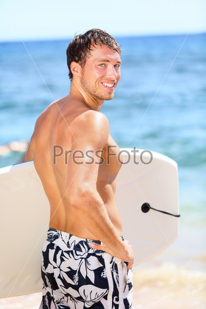 Handsome male surfer portrait on summer beach. Bodyboarding surfing man good looking standing with bodyboard surfboard during vacation holidays getaway. Caucasian water sport model in his 20s.