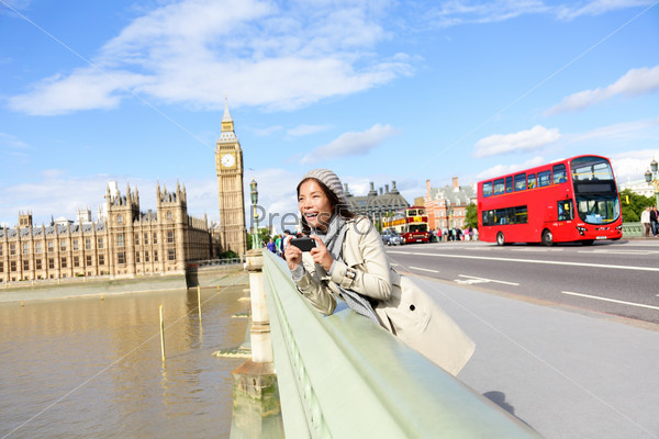 London travel woman tourist by Big Ben and red double decker bus. Girl taking photo on Westminster Bridge with smart phone camera over River Thames, London, England, Great Britain, UK.