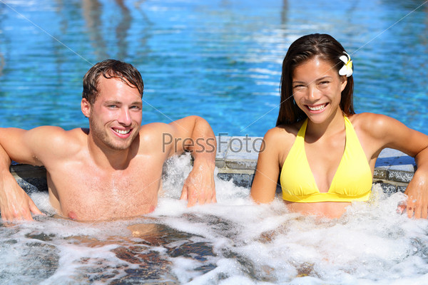 Hot tub - Couple in spa wellness jacuzzi. Portrait of beautiful young couple looking at camera on luxury resort spa retreat. Handsome man and beautiful asian woman.