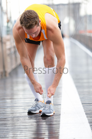 Runner man tying laces on running shoes, New York City on Brooklyn Bridge. Male athlete runner and feet closeup. Fitness model wearing compression socks.